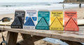 East Coast Swell surf wax lineup: five color-coded triangle bars in open cartons on a beach picnic table